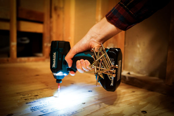 Close-up of a person using a Makita drill on a wooden surface, with a Second Set magnet attached to the side securely holding a cluster of screws, illuminated by the drill's built-in work light.