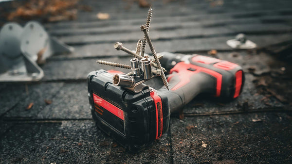 A Milwaukee drill resting on a shingled rooftop, featuring a Second Set Magnet holding screws and sockets, ideal for construction and repair work.