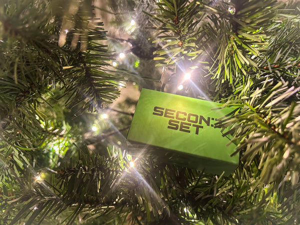 Festive green Second Set Magnets box nestled among sparkling holiday lights and evergreen tree branches, creating the perfect gift under the tree vibe.