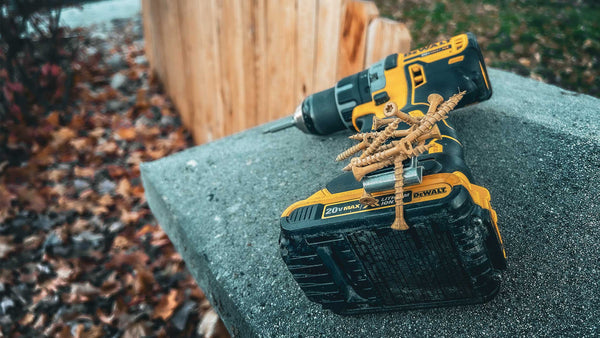 A DeWalt drill resting on a concrete surface, equipped with a Second Set Magnet securely holding several screws, with a wooden fence and fallen autumn leaves in the background.