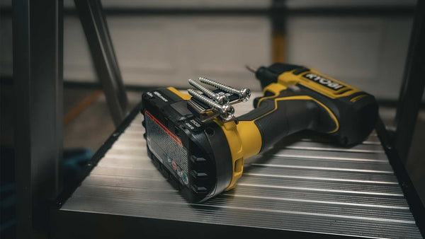 A Ryobi drill resting on a metal ladder step, equipped with a Second Set Magnet securely holding screws, showcasing its practicality for elevated projects.