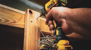 Close-up of a hand holding a DeWalt cordless drill with a Second Set magnet attached, securely holding multiple screws on the tool for efficient woodworking.